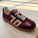 Maroon sneaker with white laces on a light-colored floor