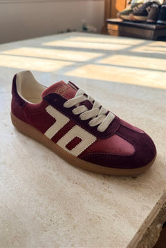 Maroon sneaker with white laces on a light-colored floor